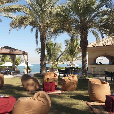 فندق شاطئ الراحة أبو ظبي المطعم الصورة The photo depicts a beautiful outdoor setting with several elements of relaxation and leisure. In the foreground, there are large, comfortable bean bag chairs arranged on a grassy area, accompanied by low tables. Surrounding this seating area are tal