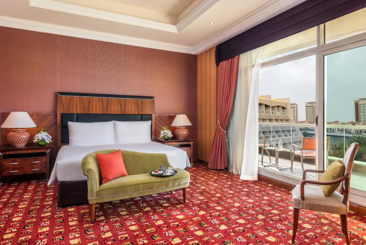 فندق شاطئ الراحة أبو ظبي المظهر الخارجي الصورة The photo shows a hotel room with an elegant and modern design. It features a large bed with white linens and a dark wooden headboard. On either side of the bed are matching bedside lamps. There is a green armchair with a red pillow positioned near t