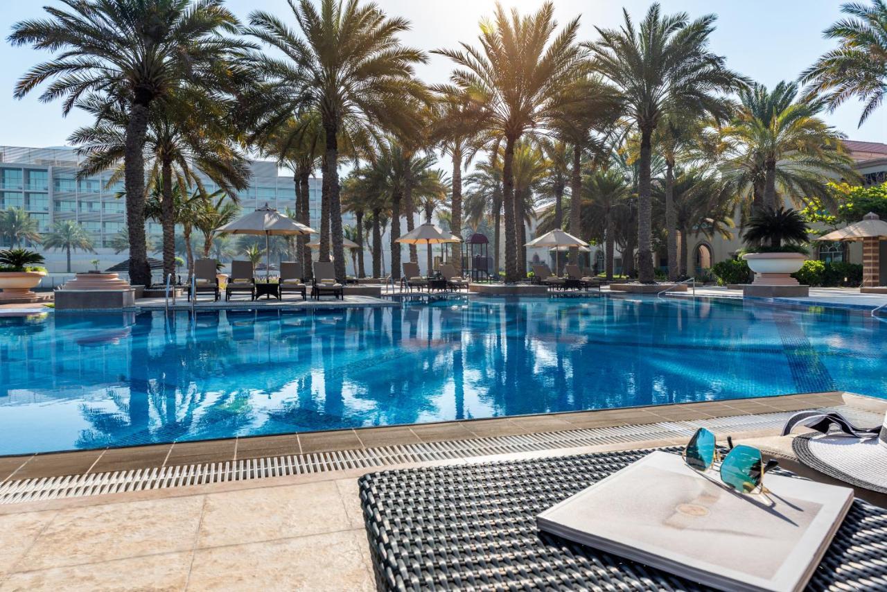 فندق شاطئ الراحة أبو ظبي المظهر الخارجي الصورة The photo shows a vibrant swimming pool surrounded by palm trees under a clear sky. The pool's water is sparkling in the sunlight, creating a serene and inviting atmosphere. Lounge chairs are placed around the pool, some of which are shaded by umbrel
