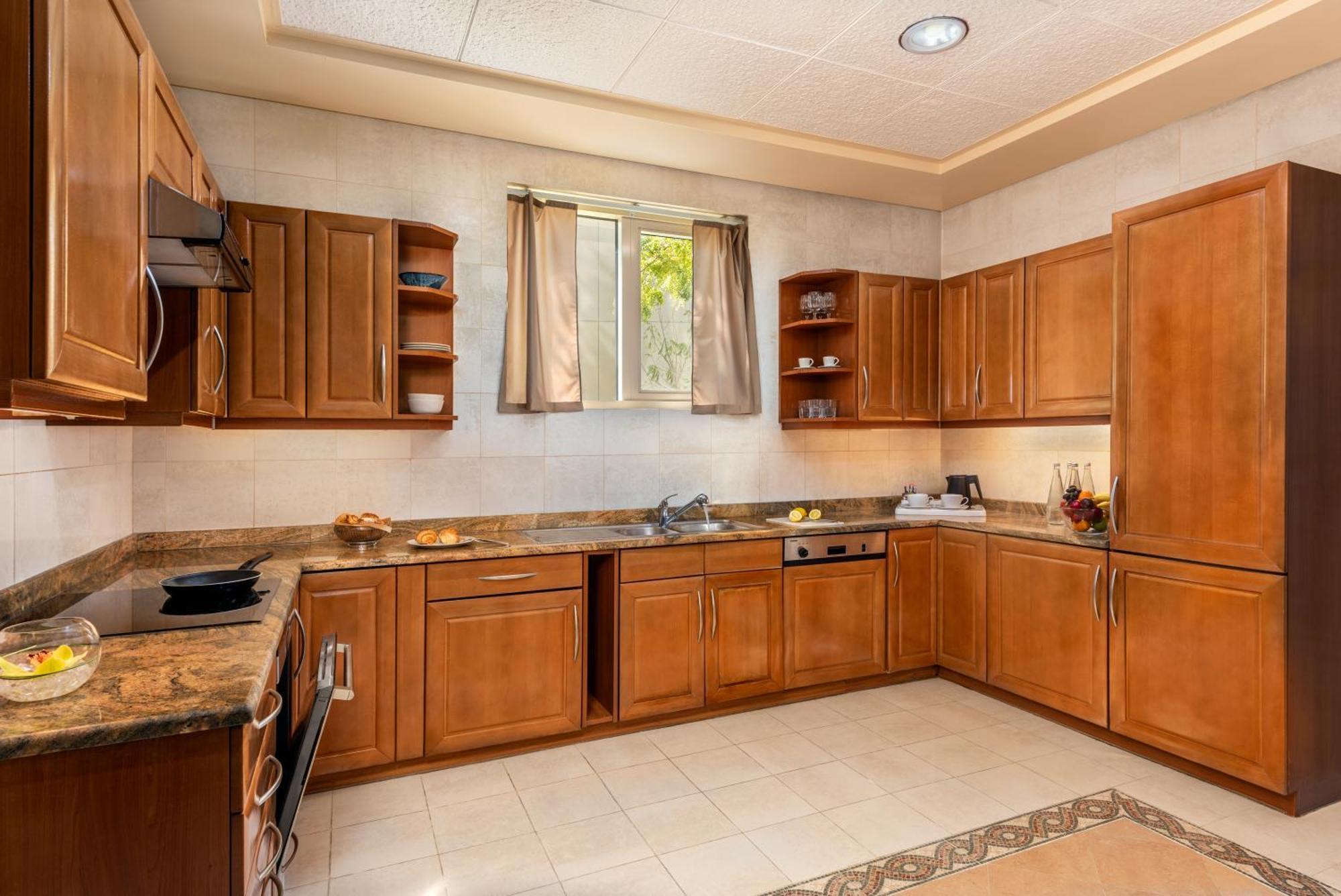 فندق شاطئ الراحة أبو ظبي المظهر الخارجي الصورة The photo shows a cozy kitchen featuring wooden cabinets with a rich brown finish, providing a warm and inviting atmosphere. The countertops are made of a light-colored stone, complementing the cabinetry. There is a window above the sink, allowing na