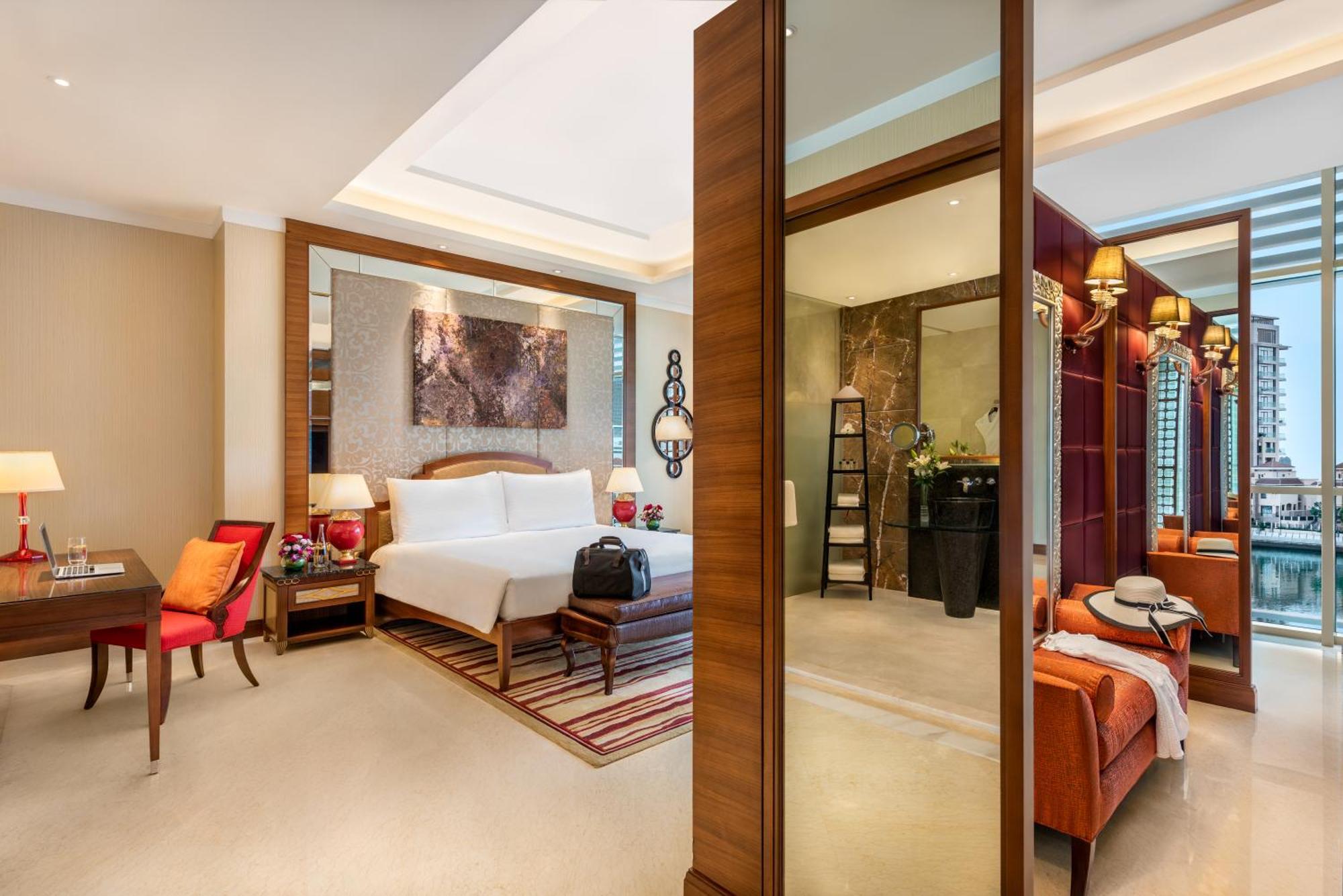 فندق شاطئ الراحة أبو ظبي المظهر الخارجي الصورة The photo shows a luxurious hotel room with a modern design. The room features a large bed with white linens, flanked by bedside tables with lamps. There is a area with a chair and a small table on the left side, and a vibrant artwork hanging above t