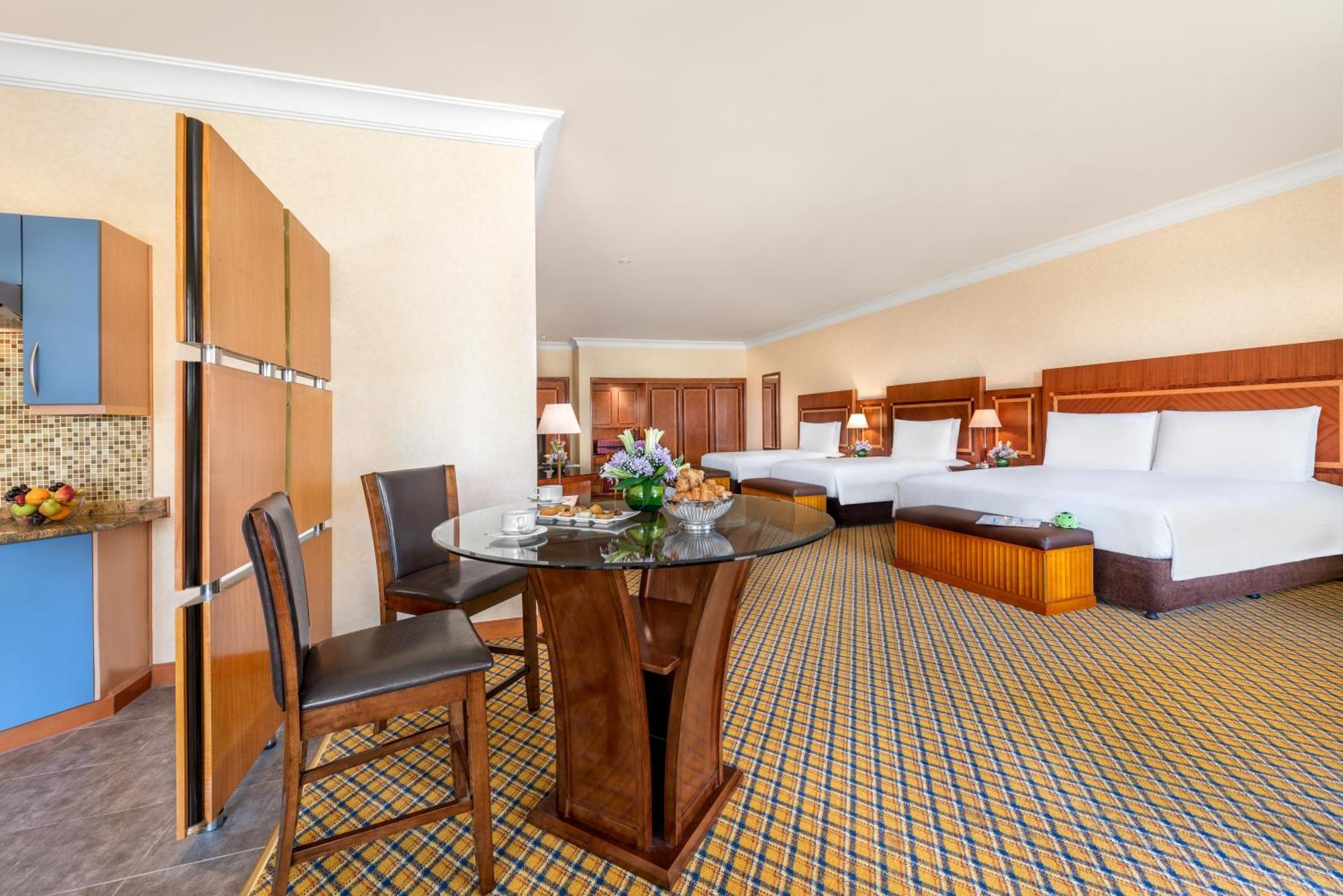 فندق شاطئ الراحة أبو ظبي الغرفة الصورة The photo displays a spacious hotel room. It features two large beds with white bedding, a circular glass dining table with a decorative floral centerpiece, and a couple of chairs around it. There is a wooden cabinet along one wall, and the room has 